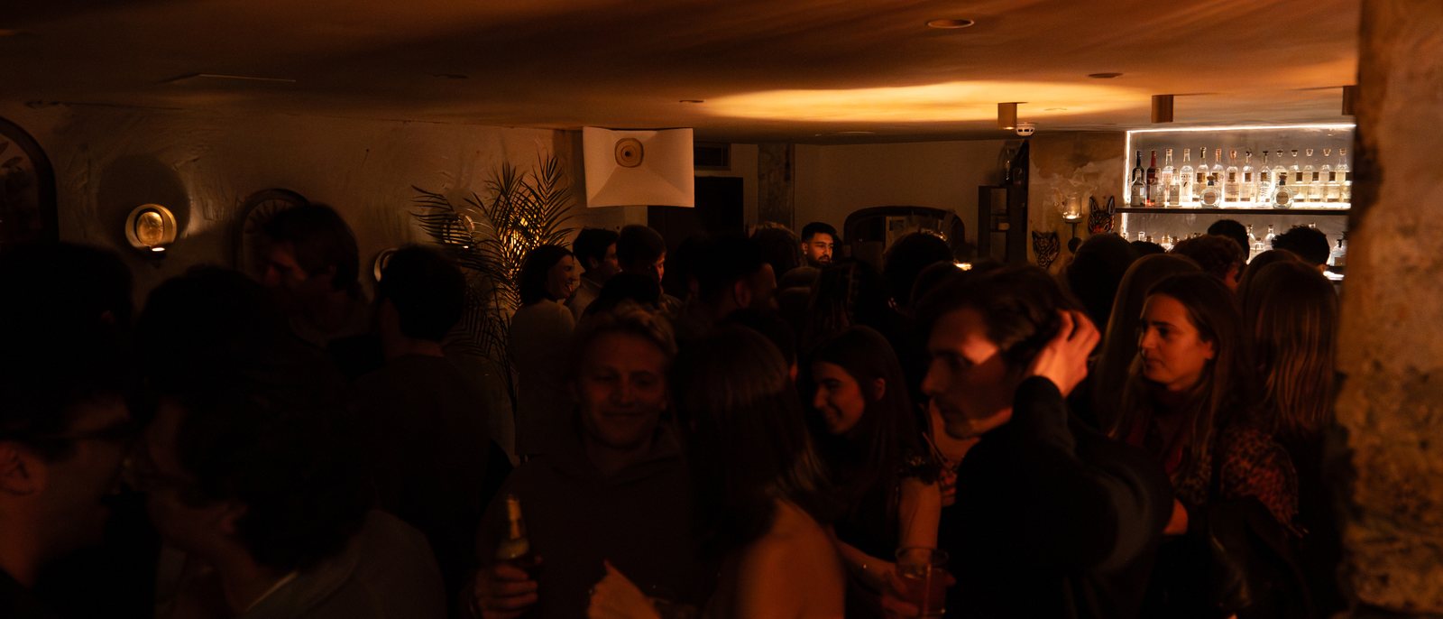 The MAYA room full, standing, the bar lit at the back.